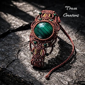 Peut inclure: Un bracelet macramé fait à la main avec une grosse pierre de malachite polie. Le bracelet est fait avec un cordon marron et des petites perles vertes et dorées. Le texte "Tricia Creations" est visible.
