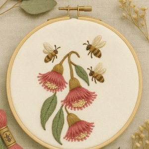 May include: Embroidered artwork in a wooden hoop, depicting pink and yellow flowers, green leaves, and three bees. The design is on cream fabric. The text "Sarah & Bee Designs" is at the bottom of the hoop.