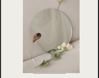 May include: A white background with the text "SELBSTKONZEPT REVOLUTION" in black. Below the text is a photo of a round mirror with a hand holding a smaller mirror in front of it. The reflection of the hand is visible in the larger mirror. There are white flowers on a table in front of the mirror. The text "WIE DU DICH SELBST LIEBEN UND DEIN LEBEN TRANSFORMIEREN KANNST" is below the photo.