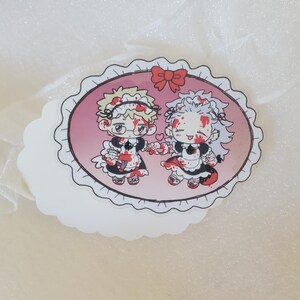 May include: A sticker featuring two cartoon characters dressed as maids, covered in blood, holding hands and smiling. The sticker is oval shaped with a pink background and a white lace border.
