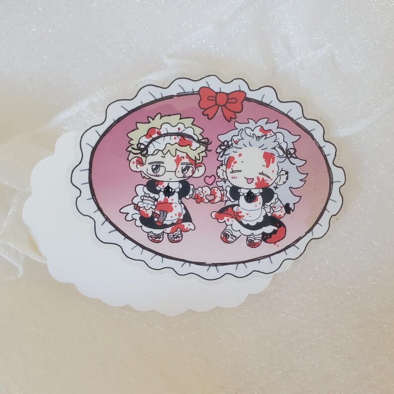 May include: A sticker featuring two cartoon characters dressed as maids, covered in blood, holding hands and smiling. The sticker is oval shaped with a pink background and a white lace border.