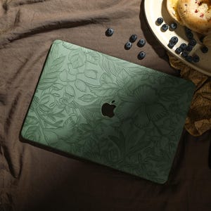 May include: A green laptop case with a floral design. The case has a subtle embossed pattern and a silver Apple logo.
