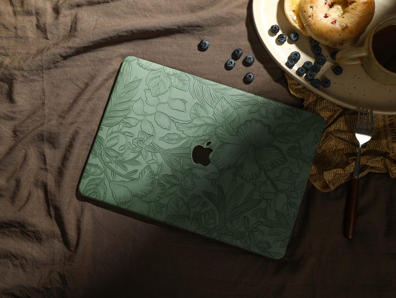 May include: A green laptop case with a floral design. The case has a subtle embossed pattern and a silver Apple logo.