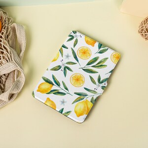 May include: A white e-reader cover with a lemon pattern. The cover features yellow lemons, green leaves, and white flowers on a white background.