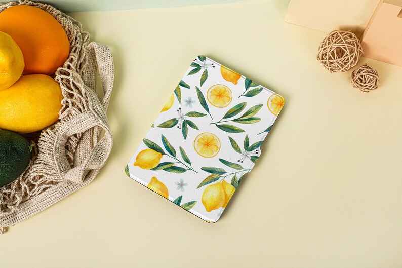 May include: A white e-reader cover with a lemon pattern. The cover features yellow lemons, green leaves, and white flowers on a white background.