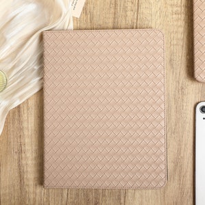 May include: A light beige woven leather laptop sleeve with a subtle textured pattern. The sleeve is lying flat on a wooden surface.