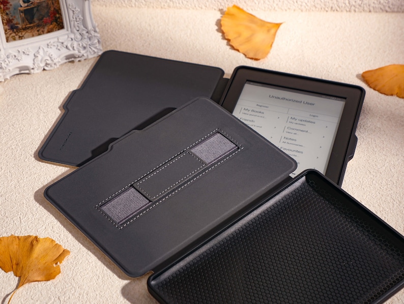 May include: A black e-reader case with a built-in stand and a strap to hold the e-reader in place. The e-reader is open and displaying a menu with the text "Library", "My Books", "My Collections", "Login", "Recent", "Settings", "Help", and "Favorites".
