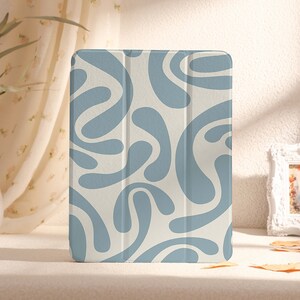 Puede incluir: Una funda para tablet con estampado blanco y azul con un diseño geométrico. La funda está hecha de un material suave y texturizado.