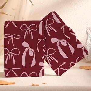 May include: Two burgundy book covers featuring a pink bow pattern. The covers are made from a soft, durable material and are ideal for protecting your favourite books.