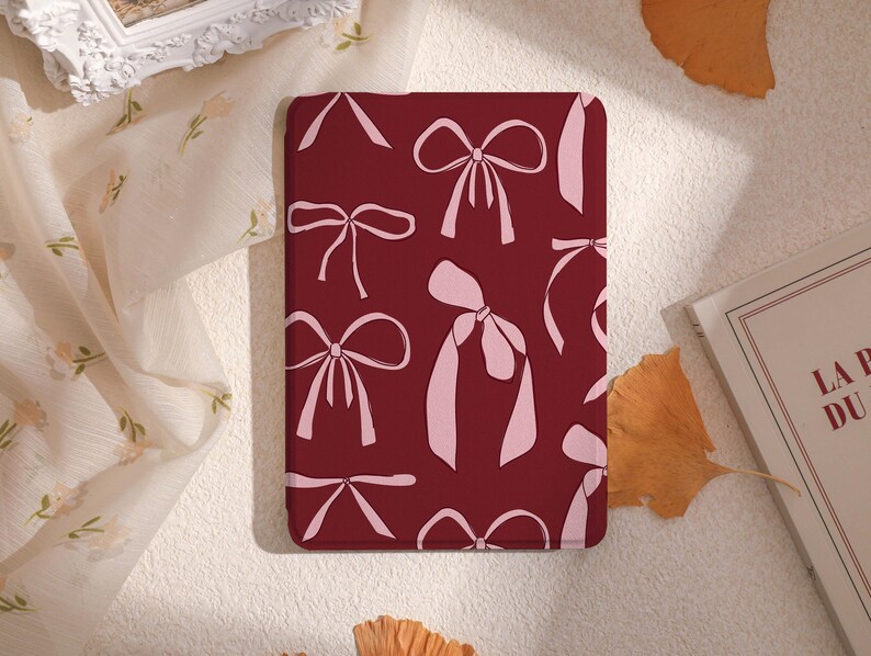 May include: A burgundy phone case with a repeating pattern of pink bows. The bows are in various sizes and orientations.