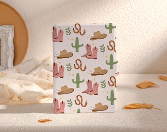 May include: A white notebook cover with a repeating pattern of pink cowboy boots, brown cowboy hats, green cacti, and orange snakes.
