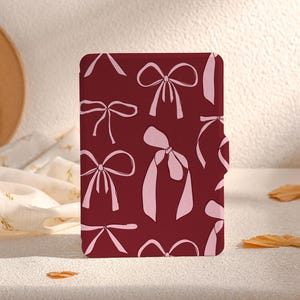 May include: A burgundy-coloured case with a pink bow pattern. The case is designed to fit an e-reader.