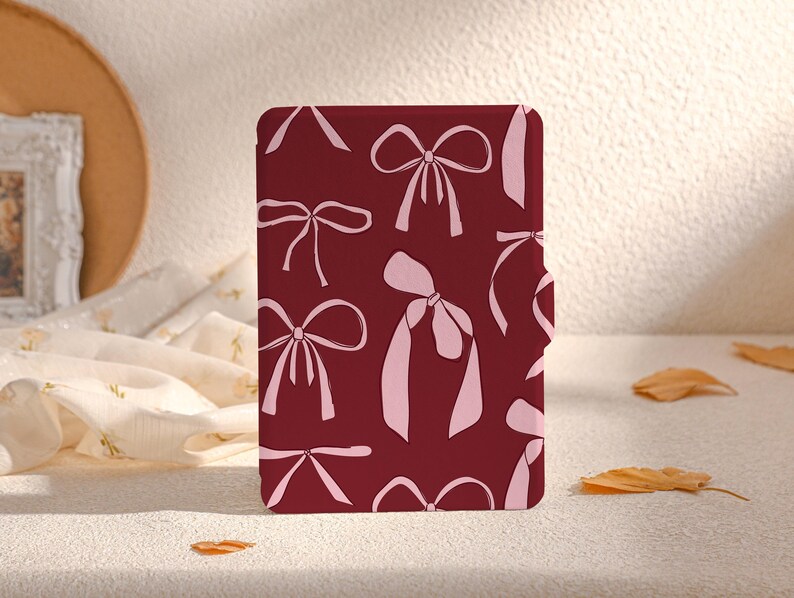May include: A burgundy-coloured case with a pink bow pattern. The case is designed to fit an e-reader.