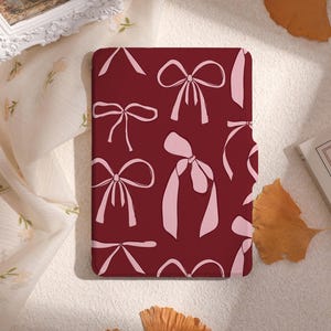 May include: A burgundy red phone case with a repeating pattern of pink bows.