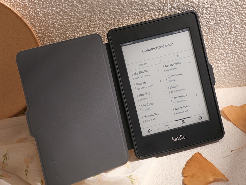 May include: A black e-reader with a screen displaying an "Unauthorized User" message. The screen shows options to register or log in, and lists various features such as "My Books", "Friends", "Reading", "My Cloud", "Vocabular", "My updates", "Comment", "Notes", "Favourites", and "Messages". The e-reader is open and has a black cover.