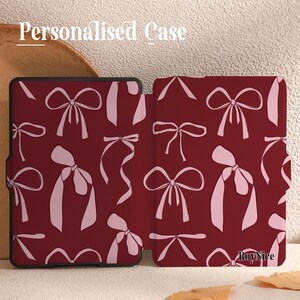 May include: A personalised case for an e-reader with a burgundy background and a pattern of pink bows. The case has the text "Roy Nice" printed on the bottom right corner.