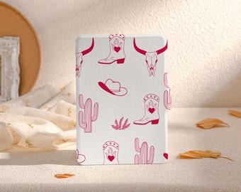 May include: A white e-reader cover with a pink and white pattern. The pattern includes cowboy boots, cacti, skulls, and hats.