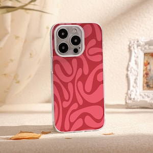 Puede incluir: Una funda transparente para teléfono con un patrón abstracto rojo. La funda tiene una protuberancia de cámara elevada con tres lentes.