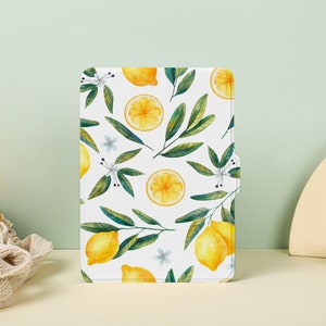 May include: A white background with a repeating pattern of yellow lemons and green leaves. The lemons are whole and sliced in half. The leaves are green and have white flowers.