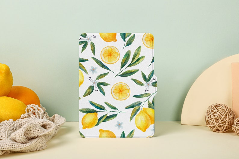 May include: A white background with a repeating pattern of yellow lemons and green leaves. The lemons are whole and sliced in half. The leaves are green and have white flowers.