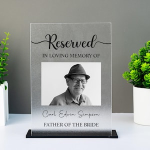 Könnte beinhalten: Ein Gedenkfoto-Display mit dem Wort "Reserved" in Schrift über einem Schwarz-Weiß-Foto eines Mannes mit Hut und Brille. Der Text "IN LOVING MEMORY OF" und "Carl Edwin Simpson FATHER OF THE BRIDE" sind ebenfalls zu sehen.