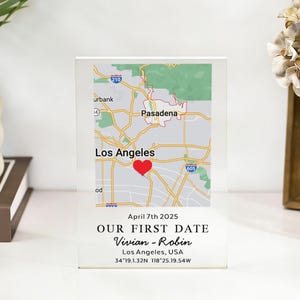 Könnte beinhalten: Ein klarer Acrylblock mit einer Karte von Los Angeles und einem roten Herz, das einen Ort markiert. Der Text "OUR FIRST DATE" und Namen stehen darunter, zusammen mit dem Datum 7. April 2025 und Koordinaten. Ein dekorativer Artikel.