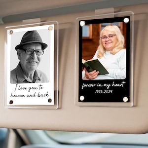 Könnte beinhalten: Zwei transparente Acryl-Fotorahmen mit Bildern von Personen, die an einer Sonnenblende befestigt sind. Ein Rahmen hat ein Schwarz-Weiß-Foto mit dem Text "I love you to heaven and back". Der andere hat ein Foto mit dem Text "forever in my heart 1936-2024."