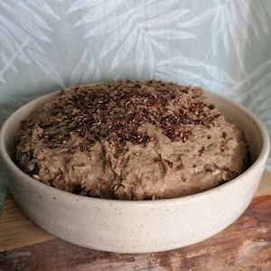 Könnte beinhalten: Nahaufnahme einer Schüssel mit braunem Teig, der mit Leinsamen bestreut ist. Die Schüssel ist aus gesprenkeltem weißem Keramik und steht auf einer Holzoberfläche.