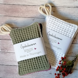 Könnte beinhalten: Zwei grüne, weiße und rosafarbene Spültücher mit Waffelstruktur. Die Spültücher haben ein weißes Etikett mit der Aufschrift "Spülschwamm Waschbar bis 60°C der Umwelt zuliebe bei 30°C Made in Thüringen".
