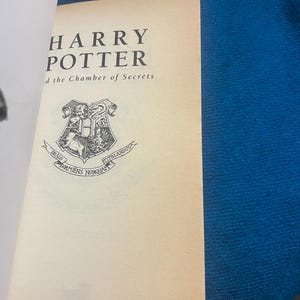 May include: A book cover for "Harry Potter and the Chamber of Secrets" with a black and white illustration of the Hogwarts crest.