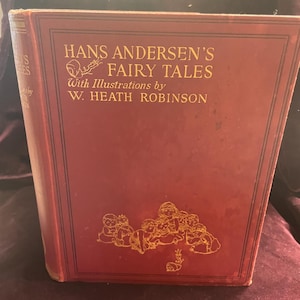 May include: A vintage hardcover book titled "Hans Andersen's Fairy Tales" with gold lettering and illustrations by W. Heath Robinson. The cover is a deep red with gold accents and a decorative illustration.