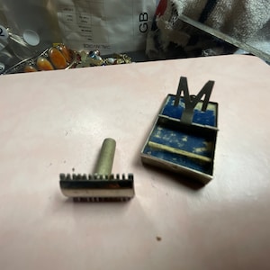 May include: A silver safety razor with a blue and silver case. The case has the letter "M" on the top.
