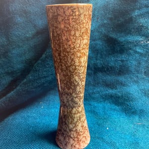 May include: A slender, vintage vase with a speckled brown and tan pattern. The vase has a flared top and a narrow waist, with a base that is a soft pink color. The vase is approximately 8 inches tall.