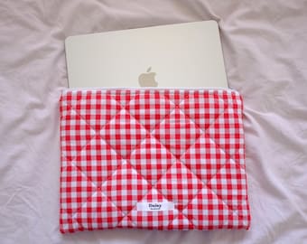 May include: Red and white gingham laptop sleeve with a quilted design. The sleeve has a white label with the word "Daisy" printed on it.