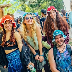 May include: A group of people wearing colorful crocheted mushroom hats. The hats are all different colors and designs. Some of the people are holding drinks.