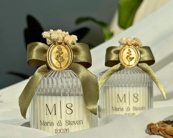Puede incluir: Dos velas en frascos de vidrio estriado transparente con una etiqueta blanca que muestra las iniciales M|S, los nombres Maria & Steven y la fecha 12.10.26. Cada frasco tiene una cinta de satén verde oliva, un sello de cera dorado y flores secas.