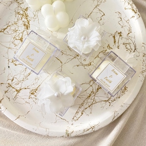 May include: Clear plastic boxes with white flowers and a white candle inside. The boxes have a label with the text "Irem & Fatih 01.05.2023".