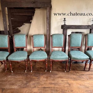 May include: Six antique wooden chairs with a teal fabric seat and back. The chairs have turned legs and a carved design on the back.