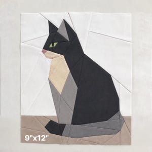 May include: A geometric fabric art piece featuring a seated cat. The cat is primarily black, with gray, beige, and white accents. The cat's eyes are green, and its nose is pink. The artwork measures 9" x 12".
