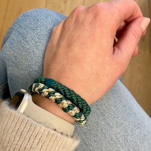 Könnte beinhalten: Nahaufnahme eines Handgelenks, das zwei Armbänder trägt. Die Armbänder sind aus grünem und goldenem Seil gefertigt. Die Armbänder sind übereinander gelegt.