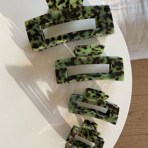 Op de afbeelding: Set van vier groene en zwarte schildpadhaarclips. De clips zijn van verschillende grootte en hebben een rechthoekige vorm met een gebogen bovenkant.