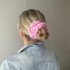 Könnte beinhalten: Eine Frau mit blonden Haaren trägt ein hellblaues Jeanshemd mit einem rosa-weiß gestreiften Haargummi im Haar.
