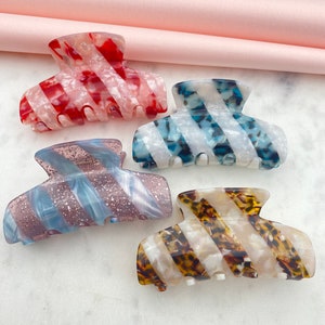 Può includere: Quattro mollette per capelli con diversi motivi a strisce. Le mollette sono realizzate in materiale plastico trasparente con un design a spirale. I motivi includono rosso e bianco, blu e bianco, marrone e bianco e rosa e bianco.