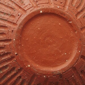 Puede incluir: La parte inferior de una maceta de terracota con un esmalte liso de color marr&oacute;n rojizo. La maceta tiene un dise&ntilde;o decorativo acanalado alrededor del borde.