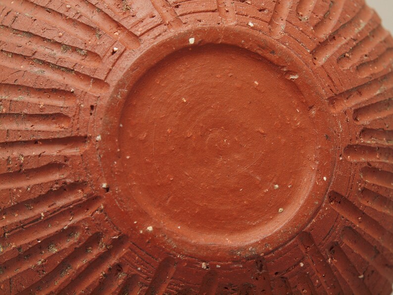 Puede incluir: La parte inferior de una maceta de terracota con un esmalte liso de color marr&oacute;n rojizo. La maceta tiene un dise&ntilde;o decorativo acanalado alrededor del borde.
