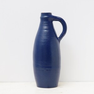 Op de afbeelding: Een donkerblauwe keramische vaas met een rond lichaam en een enkele handgreep. De vaas heeft een getextureerd oppervlak en een licht uitlopende opening.