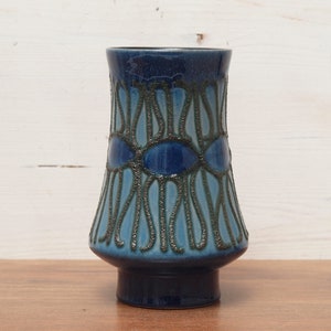 Könnte beinhalten: Eine blaue Keramikvase mit ausgestellter Form und dunklem Sockel. Die Vase hat ein strukturiertes Muster in Blau- und Türkistönen mit dunklen Konturen. Die Vase ist etwa 20 cm hoch.
