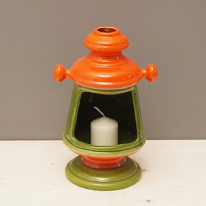 May include: A ceramic candle holder shaped like a lantern with a green and orange glaze. The lantern has a small opening for a candle and a wide base.