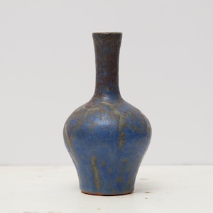 Peut inclure: Un vase en céramique fait à la main avec un glaçage bleu et marron. Le vase a un corps arrondi et un long col fin. Le glaçage bleu a un aspect moucheté, et le vase mesure environ 20 cm de haut.