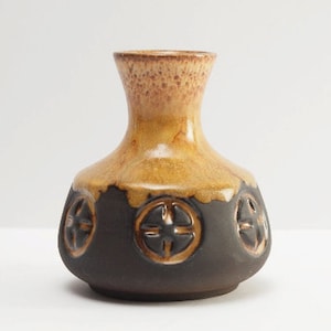 May include: A small, brown and yellow ceramic vase with a geometric design. The vase has a round body and a narrow neck.